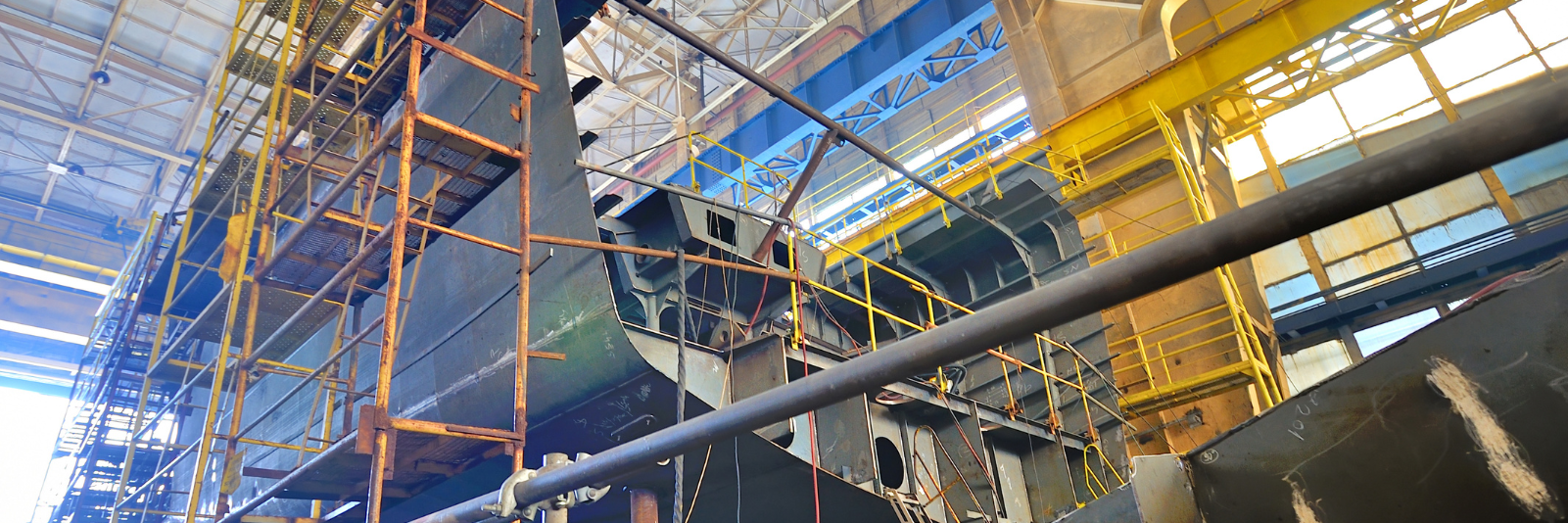 A ship hull under construction inside a shipyard fabrication hall